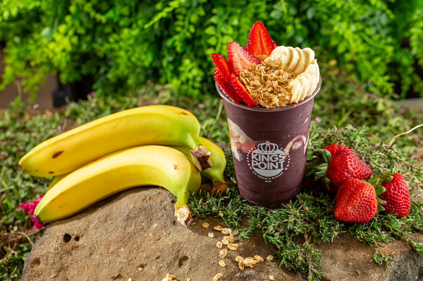 Açaí cup surrounded by fresh bananas and strawberries